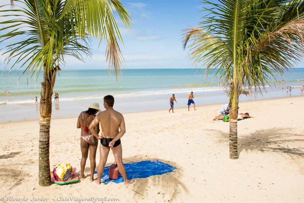 Imagem de uma casal na sombra de um coqueiro na Praia de Taperapuan.